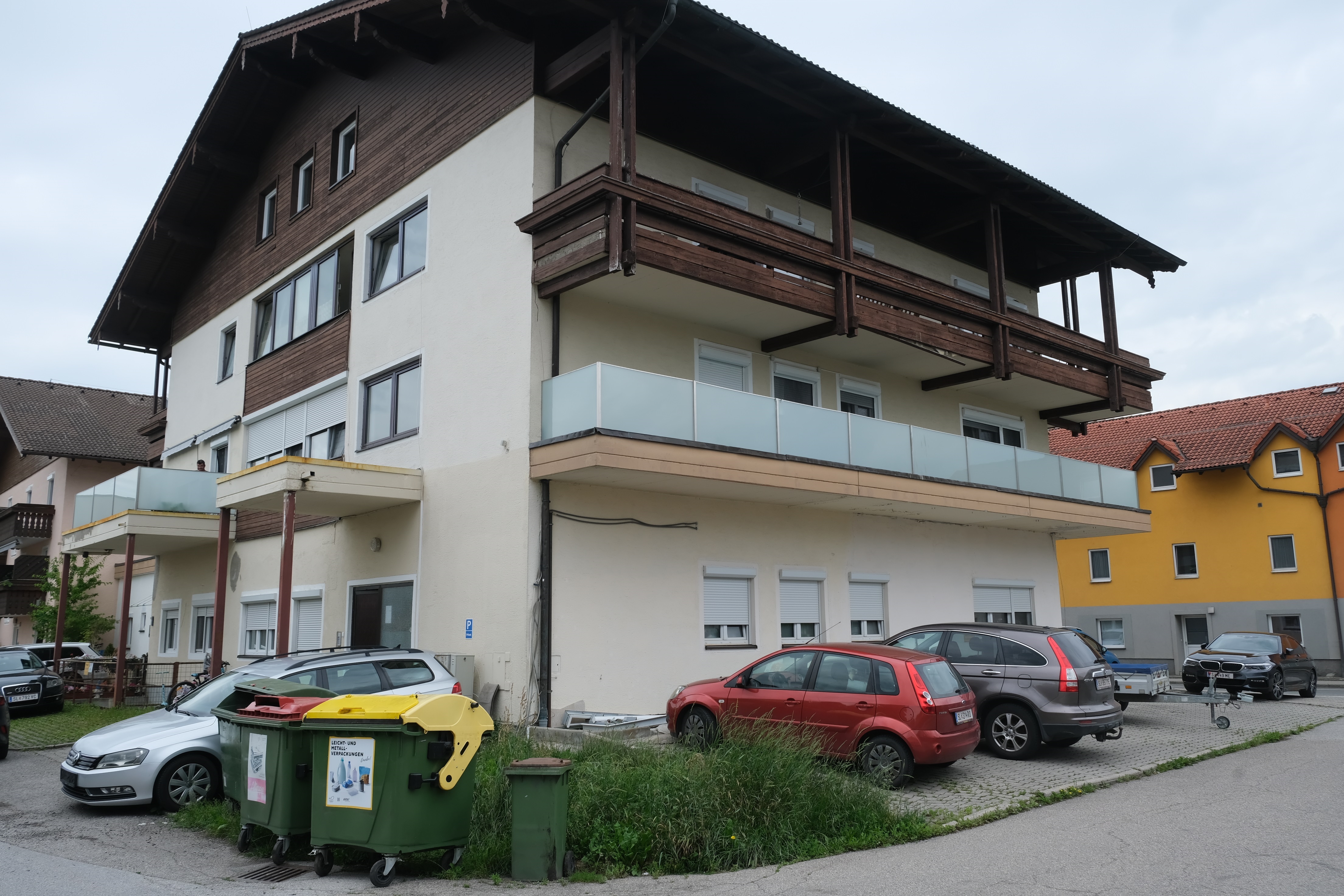 Mehrere Autos und Mülltonnen vor einem Mehrfamilienhaus mit Holzbalkonen in Österreich