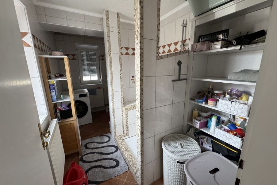 Badezimmer mit Waschmaschine, Dusche, Regal und Wäschekörben