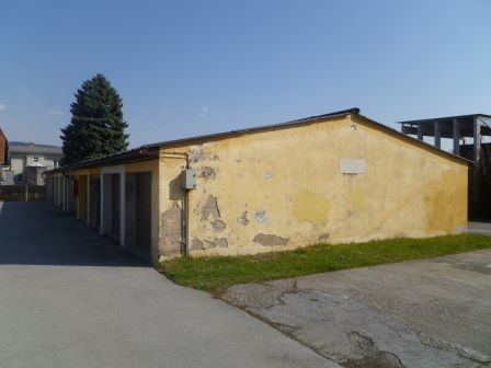 Garagenreihe in Gelb mit abblätternder Farbe, daneben eine grüne Baumspitze