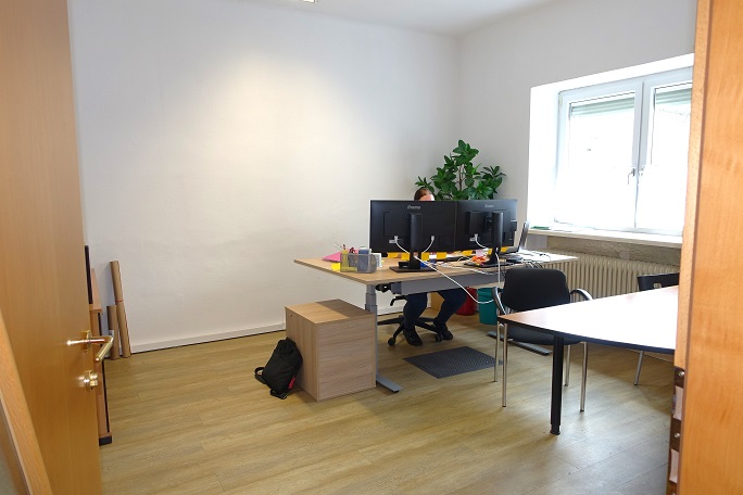 Büro mit zwei Monitoren und einer Person, die am Schreibtisch sitzt, in einem modernen Büro.