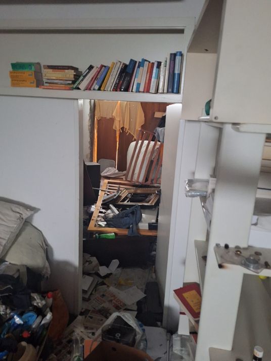 Chaos im Zimmer: Bücherregal, Bett und Boden mit Gerümpel und Papier übersät.