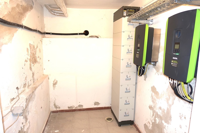 Batteriespeicher und Wechselrichter in einem Technikraum mit Rohren und Kabeln an der Wand