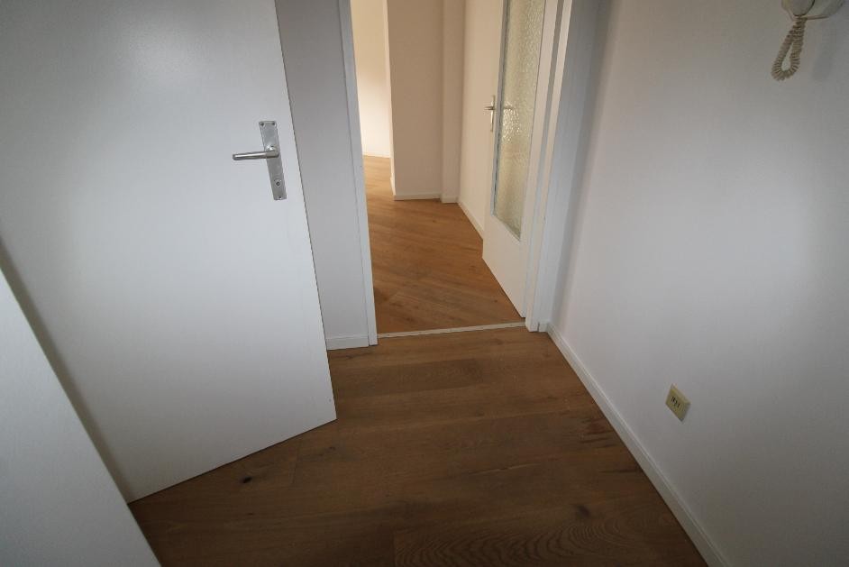 Flur mit Holzboden und weißen Türen, eine davon offen, in einem modernen Wohnraum.