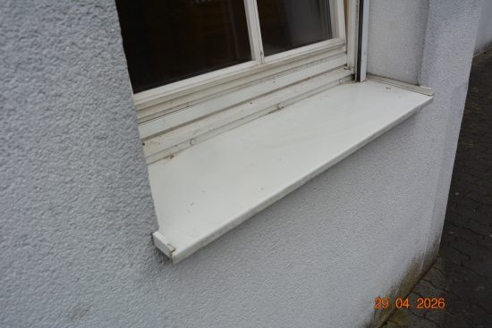 Fensterbank aus weißem Blech an einer grauen Hauswand mit strukturiertem Putz