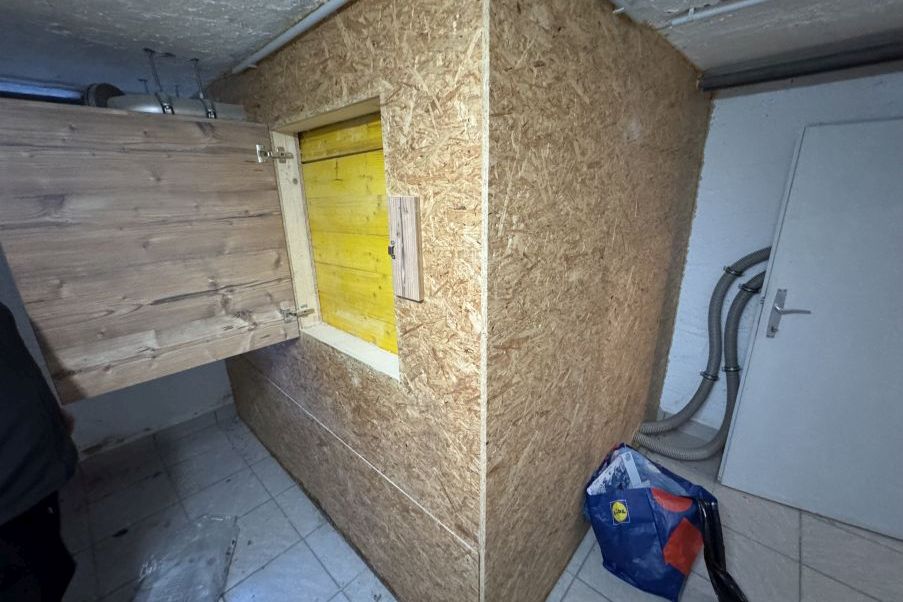 Holzkonstruktion mit gelber Tür in Kellerraum mit Lüftungsschläuchen