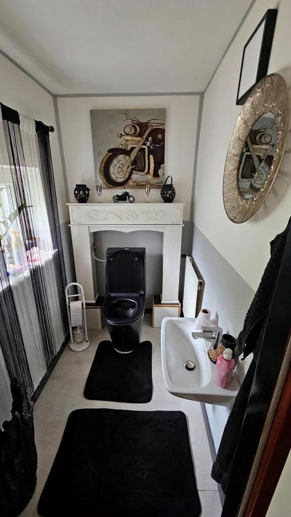 Badezimmer mit schwarzer Toilette, Waschbecken und Motorradbild an der Wand.