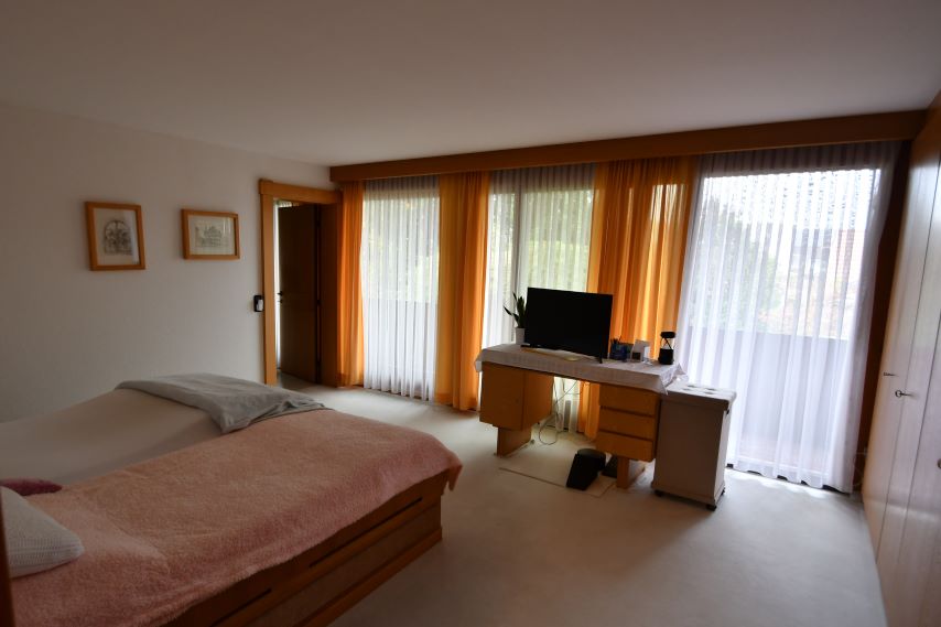 Schlafzimmer mit zwei Betten, Schreibtisch und Fernseher vor orangen und weißen Vorhängen