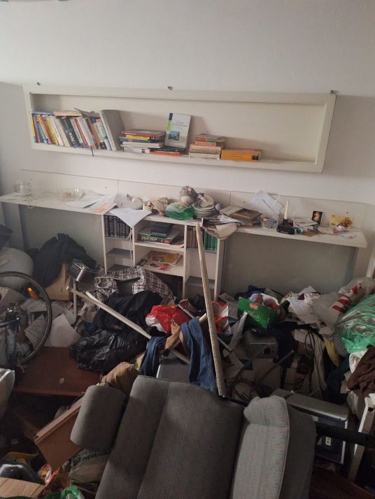 Chaos in einem Wohnzimmer mit überfüllten Regalen und am Boden liegenden Gegenständen.