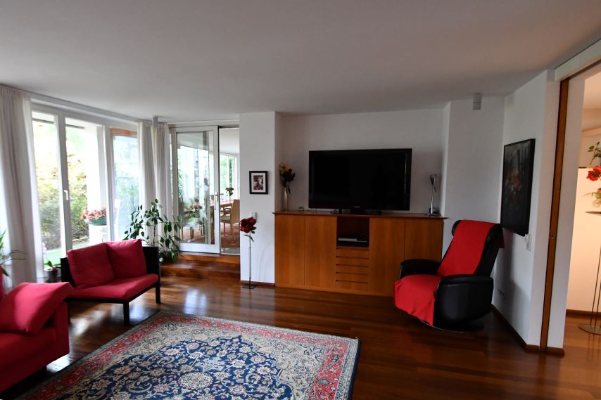 Wohnzimmer mit roten Sitzmöbeln, einem Teppich und einem Fernseher