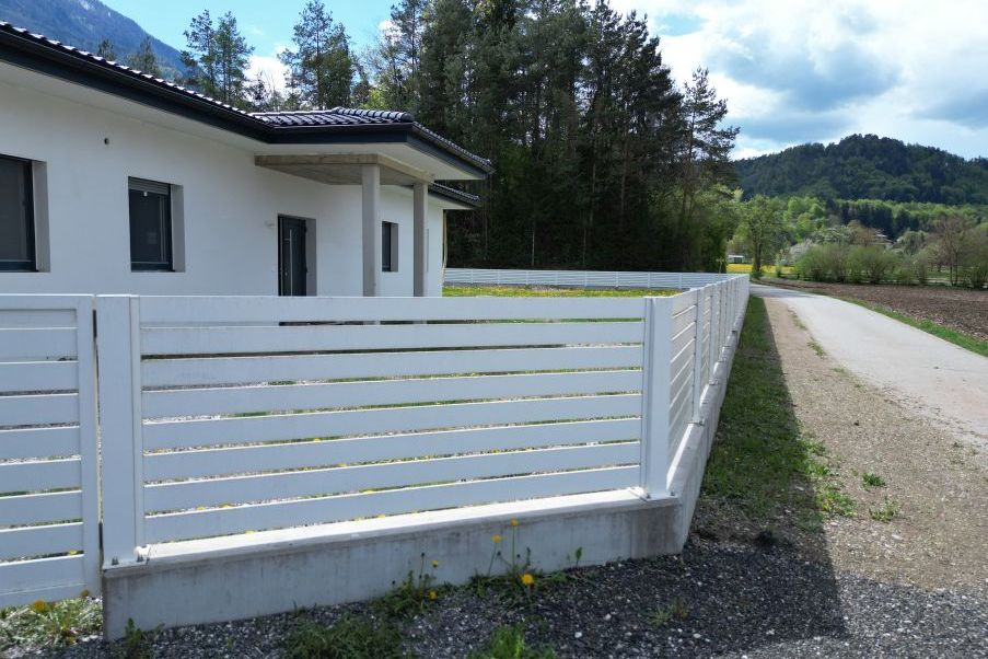 Neubau mit weißem Lattenzaun in ländlicher Umgebung vor Bergkulisse