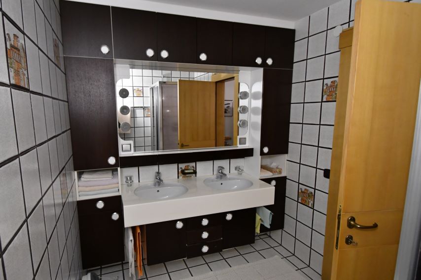 Badezimmer mit Doppelwaschbecken, Spiegel und dunklen Schränken