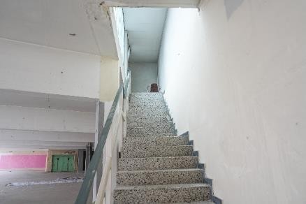 Treppenhaus mit Granitstufen und Handlauf, im Hintergrund zwei grüne Türen