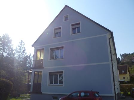 Hausfassade mit blauen Putz und weißen Zierleisten, Balkon, rote Auto